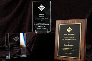Photo of three different style awards, one made of metal and wood, and two on etched glass.
